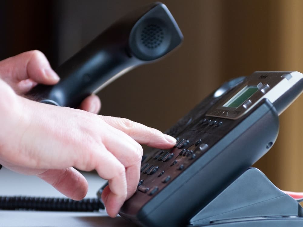 Manos de un empleado de call center marcando números en un teléfono de escritorio.